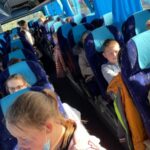 Zdjęcie przedstawia dzieci siedzących w autokarze szkolnym, w drodze do kina.