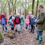Uczniowie stoją w lesie i słuchają przyrodnika