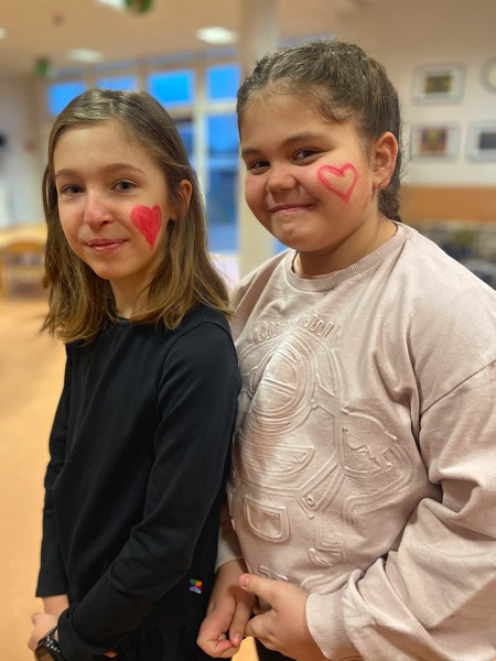 dwie uśmiechnięte dziewczynki prezentują namalowane na twarzy serduszka