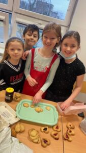 Na zdjęciu znajdują się trzy dziewczynki i jeden chłopiec, którzy prezentują swoje upieczone ciasteczkowe serca.