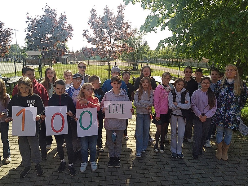 Klasa stojąca przed szkoła, dzieci trzymają napis "100-lecie"