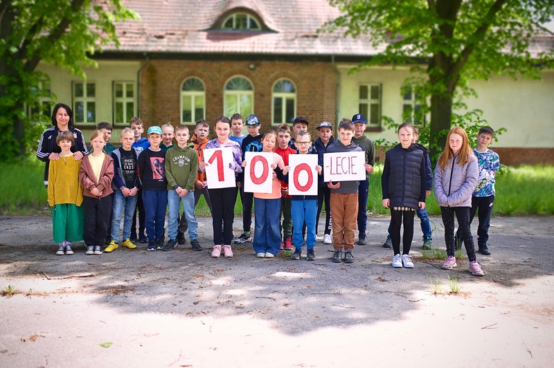 Klasa stojąca przed szkoła, dzieci trzymają napis "100-lecie"