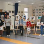 Nagrodzeni uczniowie stoja przed sztalugami, na których prezentowane są ich prace